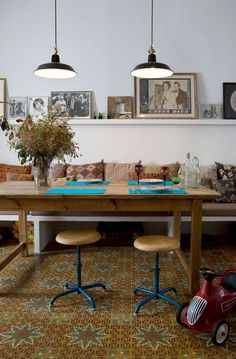 a living room filled with furniture next to a wooden table and two lamps hanging above it