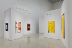 an art gallery with paintings on white walls and flooring in the center, including two large yellow abstract paintings