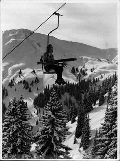 a person on a ski lift in the mountains with trees and snow covered hills behind them