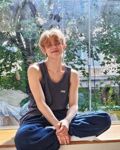 a young man sitting on top of a window sill in front of a tree