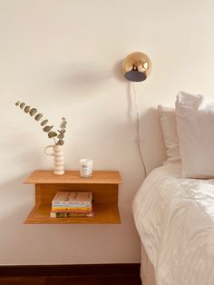 a bed with white sheets and pillows next to a wooden shelf that has books on it