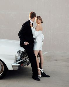 a man and woman standing next to a white car