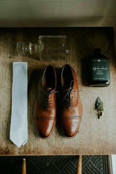 a pair of brown shoes sitting on top of a wooden table next to a white tie