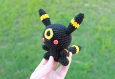 a hand holding up a small black crocheted toy with yellow eyes and ears