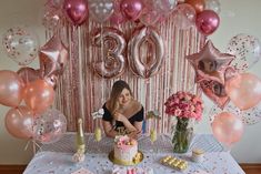 a woman sitting at a table in front of a birthday cake and balloon garlands