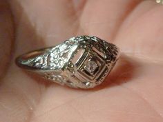 "A lovely early 19th century gold filagree ring. The under gallery is a lattice design punctuated with four blossoms and leaves.The diamond is set into a white gold diamond shape which is framed with braces on each side that are incised with circles and lines. Four rectangular openwork spaces around the setting add to its design. Ring size: 5.5 US, K 1/2 UK, 10 Japan, China, S. America Dimensions: face of ring approx. height 5/16 \" (7.94mm )of face center width 9/16 \" (14.29mm) Weight: approx. Ornate Diamond-cut Filigree Ring, Victorian Silver Filigree Ring With Diamond Accents, Victorian Platinum Filigree Jewelry, Antique Filigree Ring With Diamond Accents, Silver Filigree Art Deco Ring, Ornate Silver Filigree Diamond Ring, Ornate Filigree Diamond-cut Ring For Promise, Victorian Filigree Promise Ring With Intricate Design, Art Deco Filigree Ring For Promise