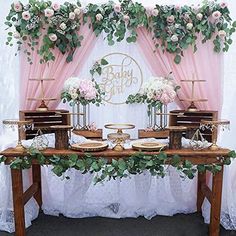 a table topped with cake and dessert covered in greenery next to a pink curtain