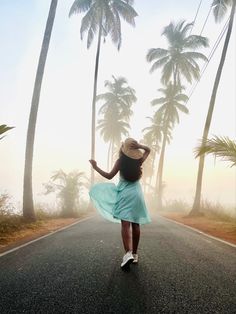 a woman in a blue dress is walking down the road with palm trees behind her