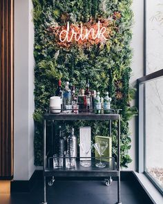 a bar cart sitting in front of a wall covered with greenery and neon signs