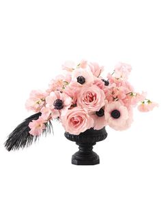 a black vase filled with pink flowers and feathers