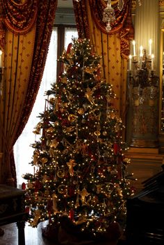 a christmas tree in the middle of a room with gold curtains and chandelier