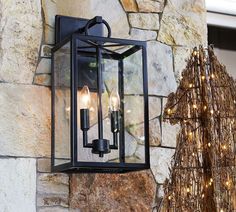 a lantern hanging from the side of a stone wall next to a christmas tree with lights on it