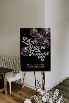 a black and white sign sitting on top of a wooden easel next to flowers