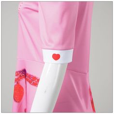 a woman's pink dress with red hearts on the collar and cuffs, from behind her is a white mannequin