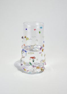 a clear glass filled with lots of different colored beads on top of a white surface