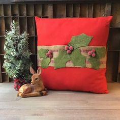 a red pillow sitting on top of a wooden floor next to a green plant and a stuffed animal