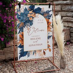 a welcome sign sitting on top of a stone floor next to purple and orange flowers