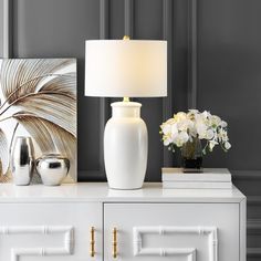 a white vase sitting on top of a dresser next to a lamp and flowers in a vase