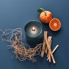 an orange, cinnamon stick and candle on a blue surface with some sticks next to it