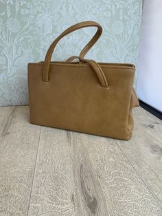 This is a stylish ladies handbag in a camel or beige leather-look material that has a smooth texture. It has a rectangular shape and a vintage look that evokes the elegance of the mid-century. The inside is lined with black satin that feels soft and luxurious. It has two side zipped pockets that are spacious and secure, and a middle section with a small zipped pocket that is perfect for storing small items. The frame, clasp and feet have gold accents that contrast beautifully with the neutral collar of the bag. The size is 28 cm wide, 16.5 cm high and 9 cm deep at the base, making it a versatile accessory that can fit many essentials.  The frame has the mark of Elbief England, a company that made frames for high quality British handbags from the 1940s to the 1970s. The mark is a sign of cr Beige Satchel With Hasp Closure For Shopping, Classic Light Brown Shoulder Bag With Double Handle, Classic Light Brown Satchel With Double Handle, Rectangular Satchel With Hasp Closure, Classic Beige Box Bag For Shopping, Beige Rectangular Bag With Hasp Closure, Beige Satchel With Hasp Closure For Office, Classic Beige Square Shoulder Bag, Classic Beige Rectangular Bag