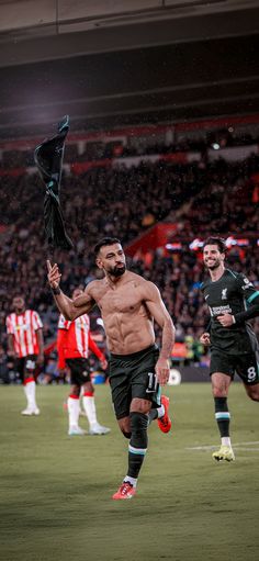 a shirtless man running on a soccer field holding an umbrella in the air with other players behind him