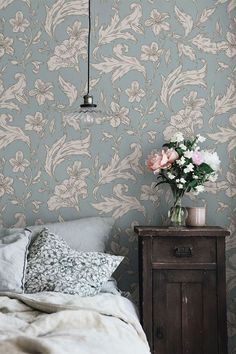 a bedroom with floral wallpaper and a wooden night stand in front of the bed