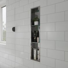 a white tiled bathroom with a window and shelf on the wall next to toiletries