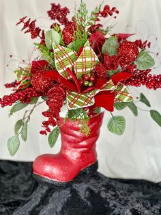 a red boot filled with flowers and greenery sitting on top of a black surface