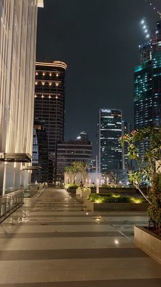 an empty walkway in the middle of a city at night with tall buildings behind it