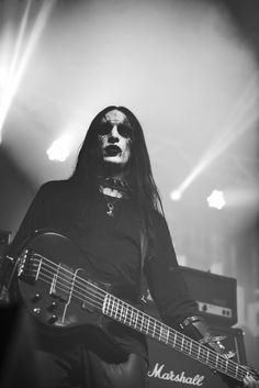 a black and white photo of a man with long hair playing an electric guitar on stage