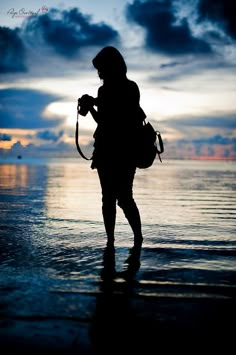 a person with a camera standing in the water at sunset or dawn, silhouetted against an overcast sky