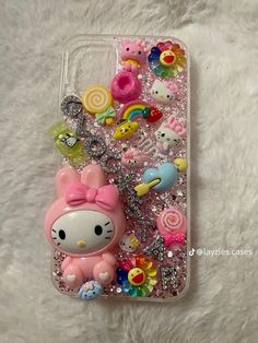 an iphone case with hello kitty and other items on it, sitting on a white surface