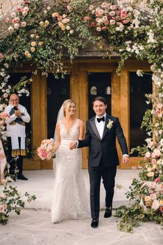 a bride and groom walking down the aisle after their wedding ceremony in front of an archway decorated with flowers