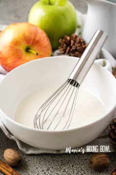 an apple and milk mixture in a white bowl next to cinnamons, apples and nuts