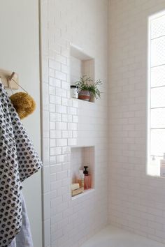 a white tiled bathroom with black and white towels hanging on the shower wall next to a bathtub