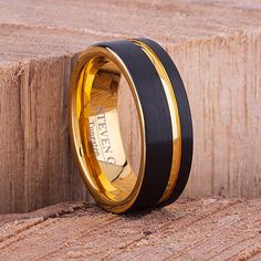 two tone gold and black wedding band with an engraved name on the inside, set against a wooden background