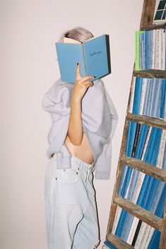 a young boy is reading a book in front of a ladder and bookshelf