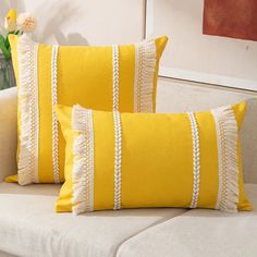 two yellow pillows sitting on top of a white couch next to a vase with flowers