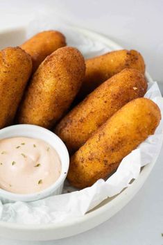 some fried food is in a white bowl with dipping sauce on the side for dipping