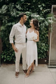 a man and woman standing next to each other in front of green plants on the wall