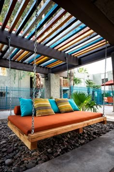 an orange swing bed with blue and yellow pillows on it in front of a house