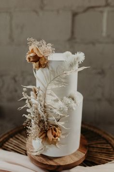 a white wedding cake with dried flowers and leaves on top is sitting on a wooden stand