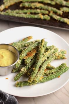 asparagus sticks on a white plate with mustard in a small bowl next to them