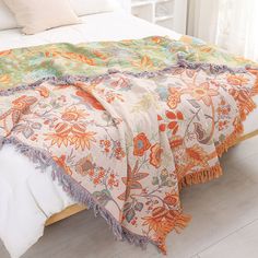 a white bed with an orange and green blanket on top of it next to a window