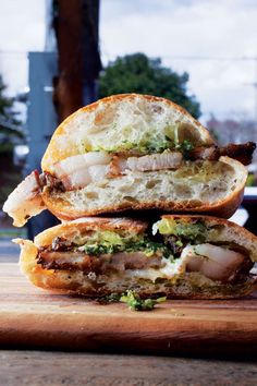 two sandwiches stacked on top of each other with meat and vegetables in the middle, sitting on a wooden cutting board