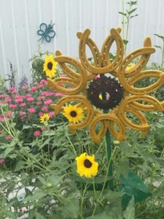 a sunflower sculpture in the middle of a garden with other flowers and plants around it