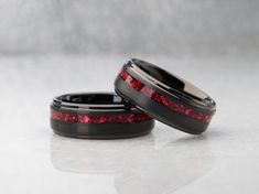 two wedding bands with red glitter in them sitting on a white surface, next to each other