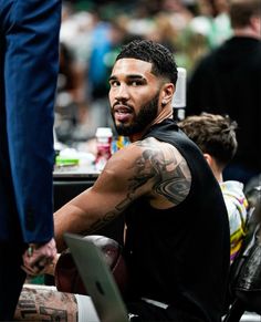 a man with tattoos on his arm sitting in front of a table and looking off to the side