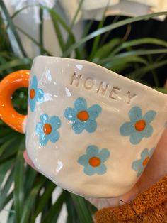 a hand holding a ceramic mug with the word honey written on it and blue flowers