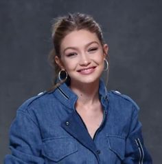 a young woman in a denim shirt smiles at the camera while wearing large hoop earrings